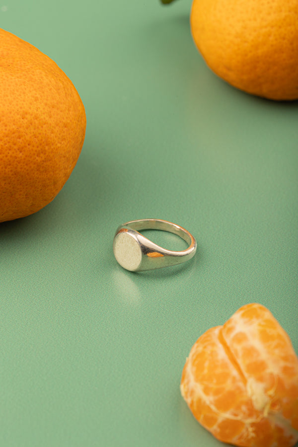 Polished silver ring with oval crest photographed on fresh orange branch