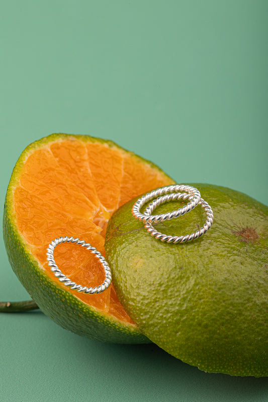 Three silver twist bands from Argenté Jewelry styled on a sliced green orange.